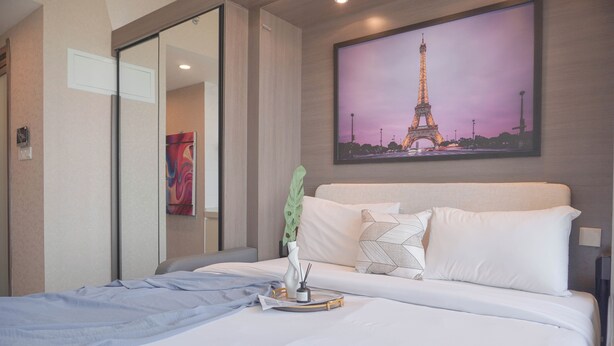 A hotel room with a bed, a painting of the Eiffel Tower, a mirror, and a green plant. - Comfort And Good Place Studio At Sky House Bsd Apartment (Pagedangan)