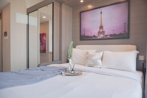 A hotel room with a bed, a painting of the Eiffel Tower, a mirror, and a green plant. - Comfort And Good Place Studio At Sky House Bsd Apartment (Pagedangan)