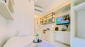A hotel room with a bed, a small kitchenette, a television, and a window. - Comfy Studio At Tokyo Riverside Pik 2 Apartment (Teluknaga)