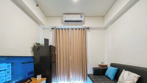 Una sala de estar moderna con un televisor de pantalla plana, un refrigerador negro, un mueble de madera, un sofá negro con cojines azul y beige, y una cortina con detalles iluminados.