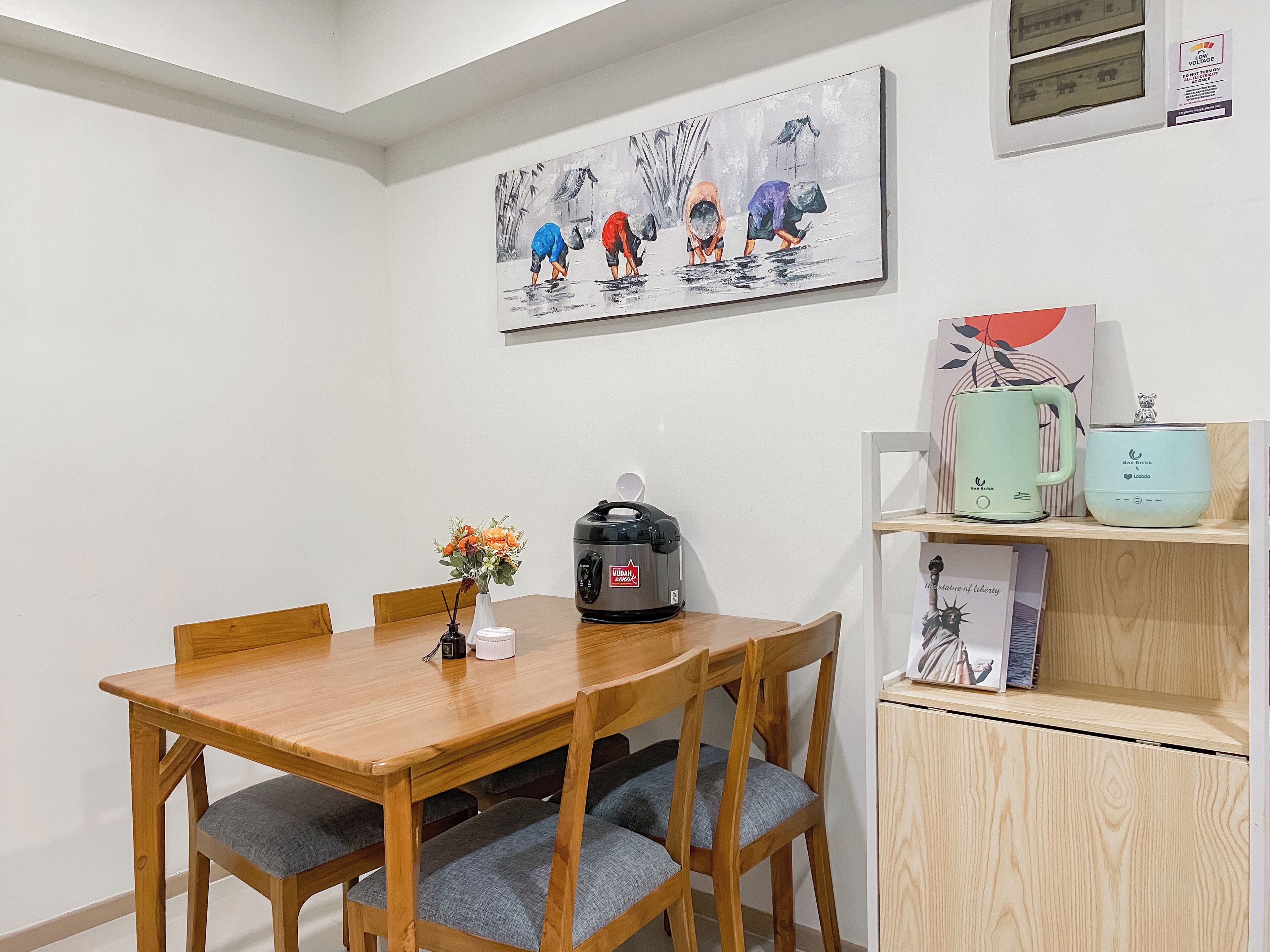 A dining area with a wooden table and chairs, a kettle, a coffee maker, and a shelf with kitchen appliances.