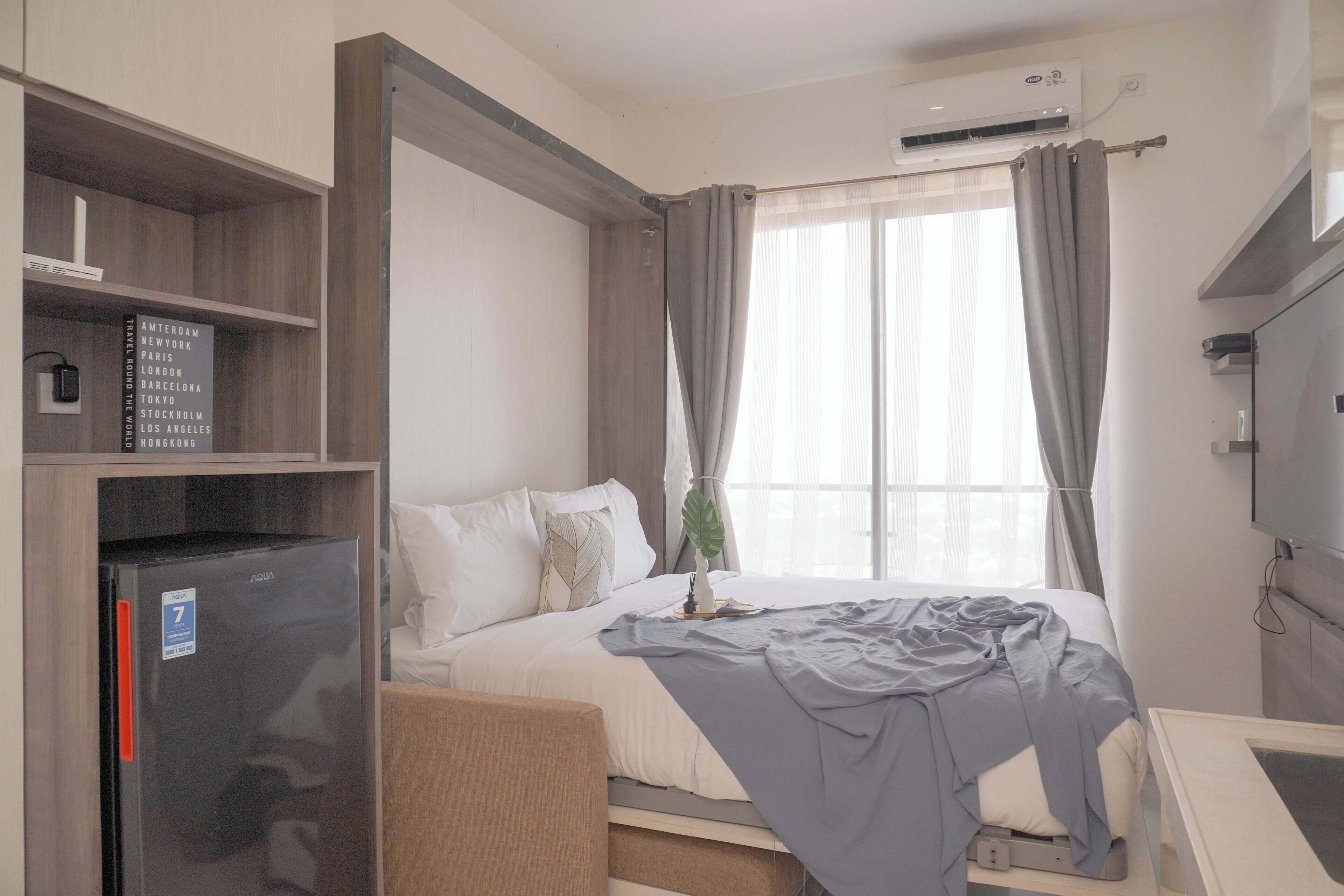 A hotel room with a bed, a desk, a refrigerator, and a window with curtains.