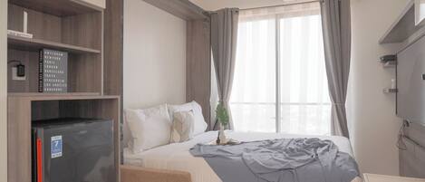 A hotel room with a bed, a desk, a refrigerator, and a window with curtains.