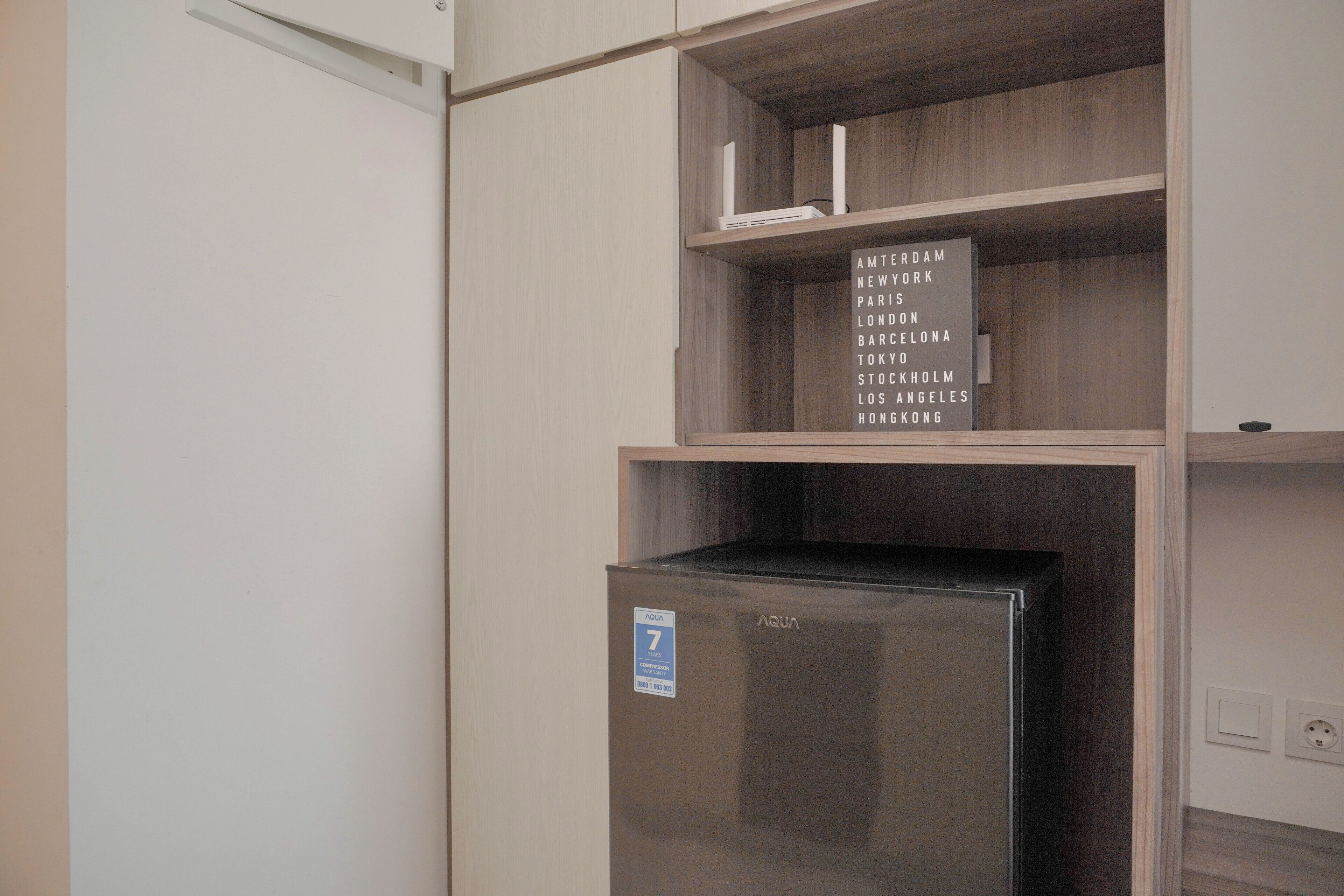 A kitchenette with a stainless steel refrigerator, wooden shelves, and a sign listing cities.