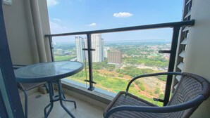 A balcony with a table and two chairs, offering a view of a cityscape with high-rise buildings and greenery. - Best Choice And Cozy Studio Sky House Bsd Apartment (Pagedangan)