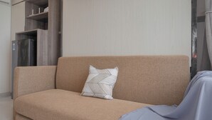 A beige sofa with a geometric-patterned pillow, a grey blanket, and a stainless steel refrigerator in the background. - Best Choice And Cozy Studio Sky House Bsd Apartment (Pagedangan)