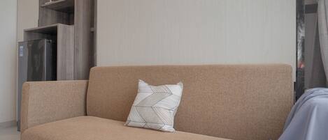 En beige sofa med en pude med geometrisk mønster, et gråt tæppe og et stålstålskøleskab i baggrunden.