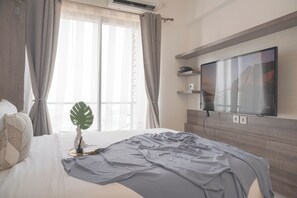 Relax in a serene space with a neatly made bed, flat-screen TV, and a potted plant.