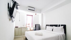 A hotel room with a bed, a desk, a chair, an air conditioner, and a TV mounted on the wall. - Restful And Tidy Studio At Paltrow City Apartment (Semarang)