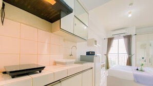 Una habitación de hotel moderna con kitchenette, un ventanal con cortinas, una cama con cubrecama blanco y un equipo de aire acondicionado.