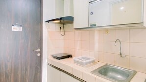 Una cocina compacta con azulejos blancos, un lavamanos de acero inoxidable y una placa de cocción por inducción negra.