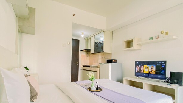 Habitación de hotel con cama, televisión, una kitchenette pequeña y un baño visible a través de una puerta abierta.