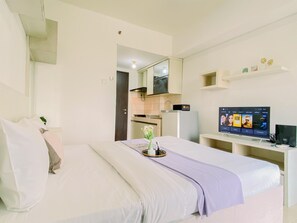 A hotel room with a bed, a TV, a small kitchenette, and a bathroom visible through an open door. - Modern And Good Deal Studio At Serpong Greenview Apartment (South Tangerang)