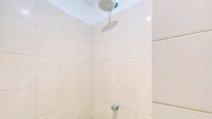 Un área de ducha con azulejos, cabezal de ducha instalado en el techo y grifo en la pared.