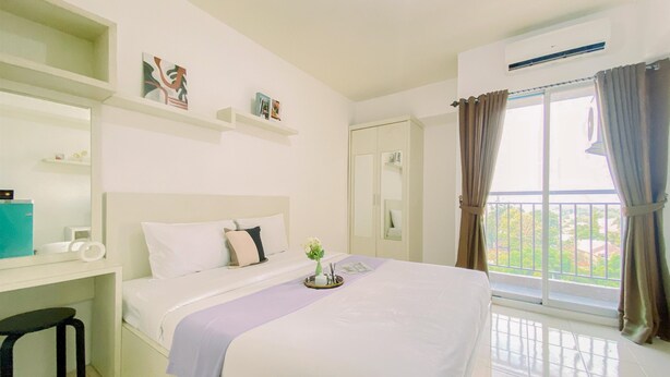 Un dormitorio con cama, escritorio, silla, armario y balcón con cortinas.