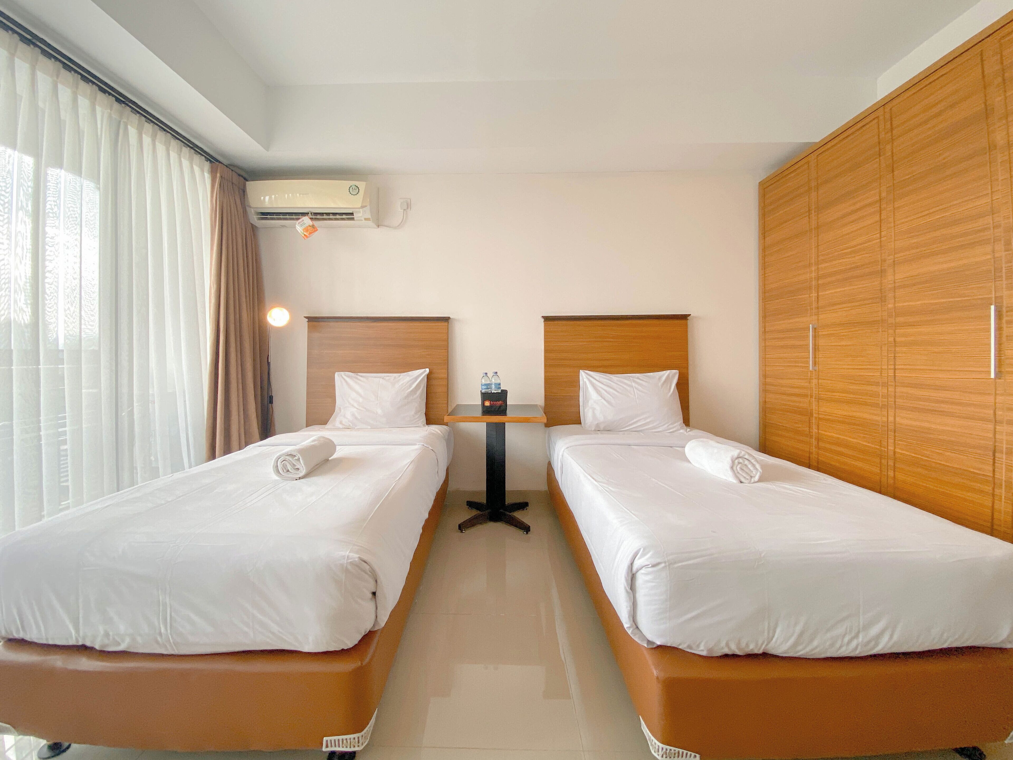 A hotel room with two beds, a small table, an air conditioning unit, and a wardrobe.