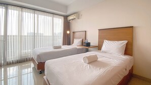 A hotel room with two beds, a bedside table, a lamp, and a window with curtains. - The Elite Enclave Studio At Beverly Dago Apartment (Bandung)