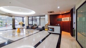 A modern hotel lobby with a reception desk, seating area, and a large window offering a view of the street. - The Elite Enclave Studio At Beverly Dago Apartment (Bandung)