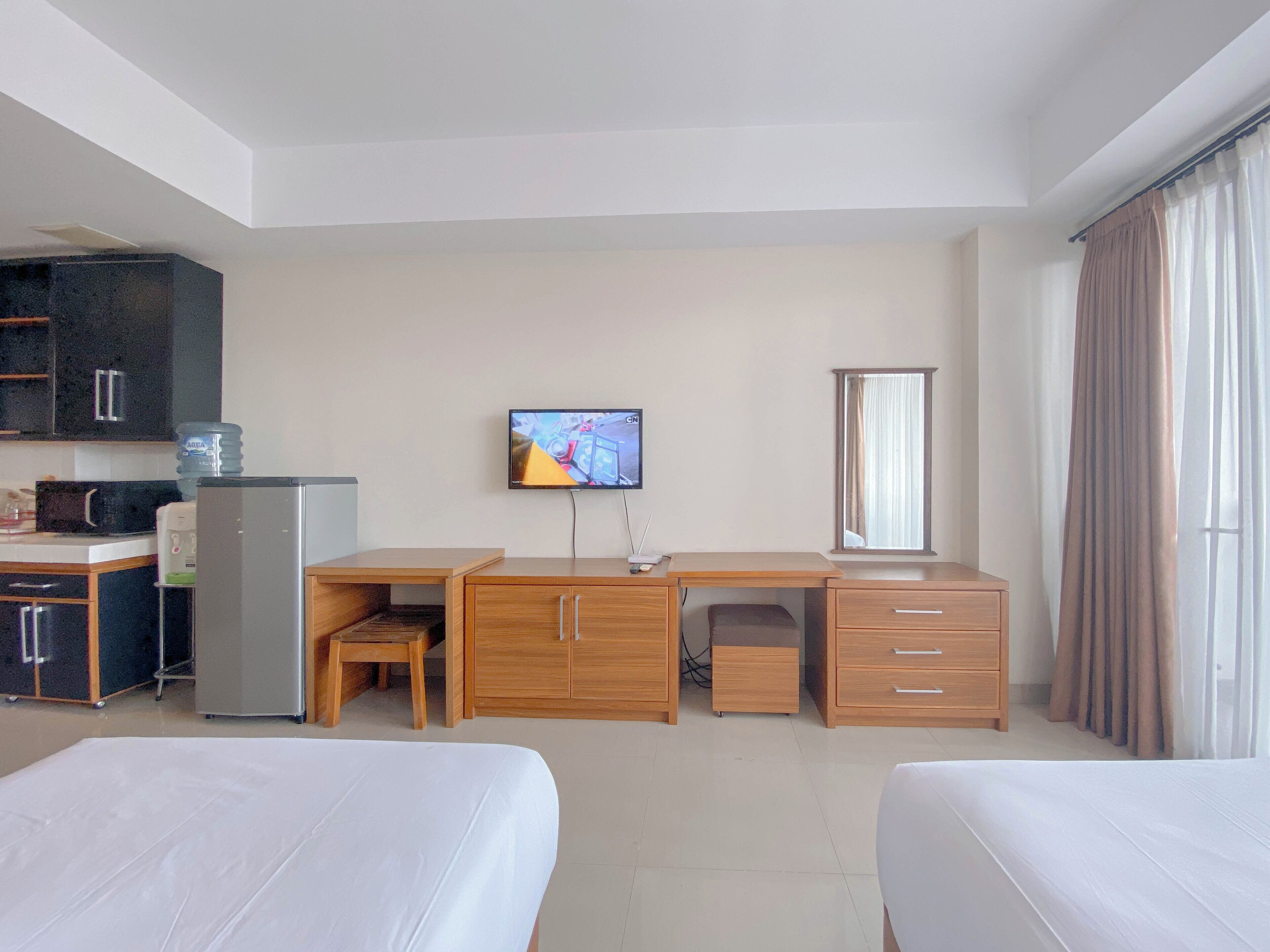A hotel room with a bed, a desk, a chair, a TV, a window, and a kitchenette.