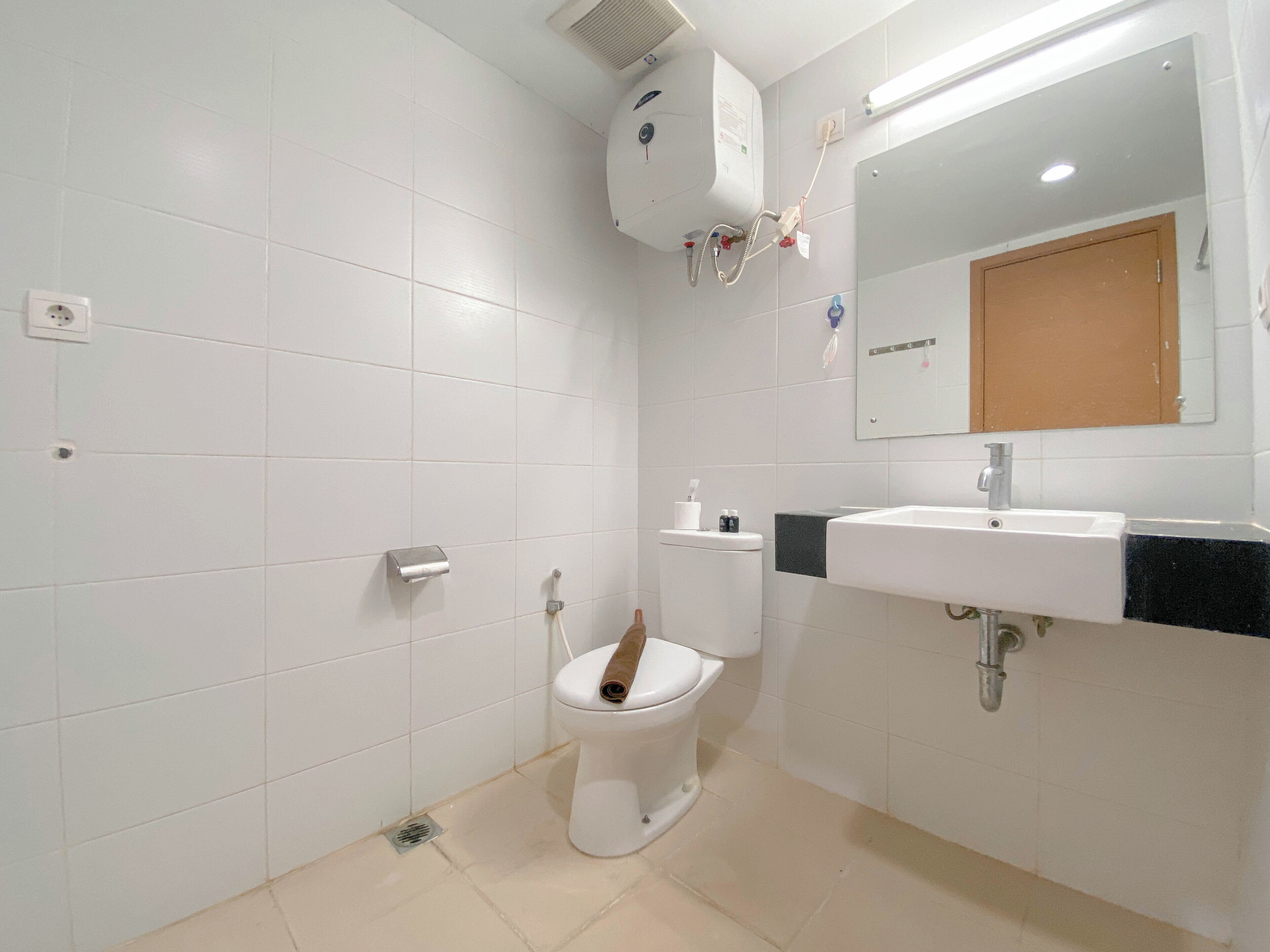 A bathroom with white tiles, a toilet, a sink, and a mirror.