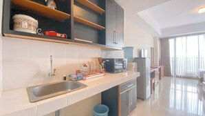 A modern kitchen with a stainless steel sink, a microwave, and a water dispenser. There are cabinets above the counter and a window with curtains. - The Elite Enclave Studio At Beverly Dago Apartment (Bandung)