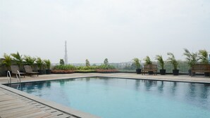 Piscina en la azotea con terraza de madera, bancos y plantas en macetas.