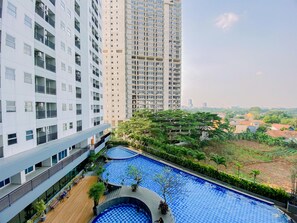 Un edificio alto con varios balcones y un área de piscina en la azotea, rodeada de vegetación.
