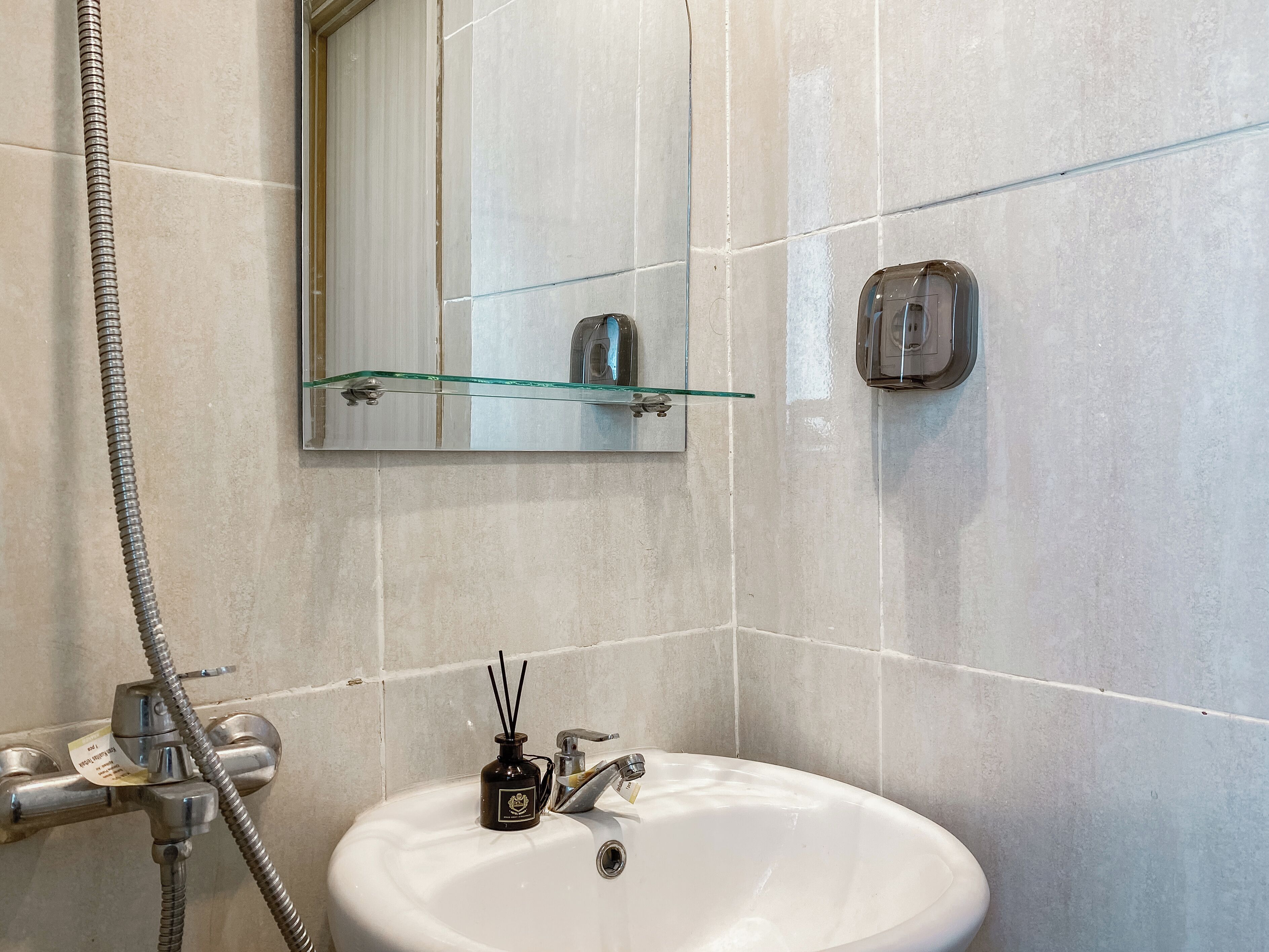 A bathroom with a white sink, a glass shelf, a mirror, and a shower hose.
