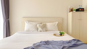 Ένα στρωμένο κρεβάτι με λευκά σεντόνια, ένα διακοσμητικό μαξιλάρι και ένα μικρό φυτό σε ένα δισκάρι.