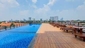 A rooftop pool with wooden deck and lounge chairs, overlooking a cityscape. - Good Studio And Comfortable 1Br At Tamansari Bintaro Mansion Apartment (South Tangerang)