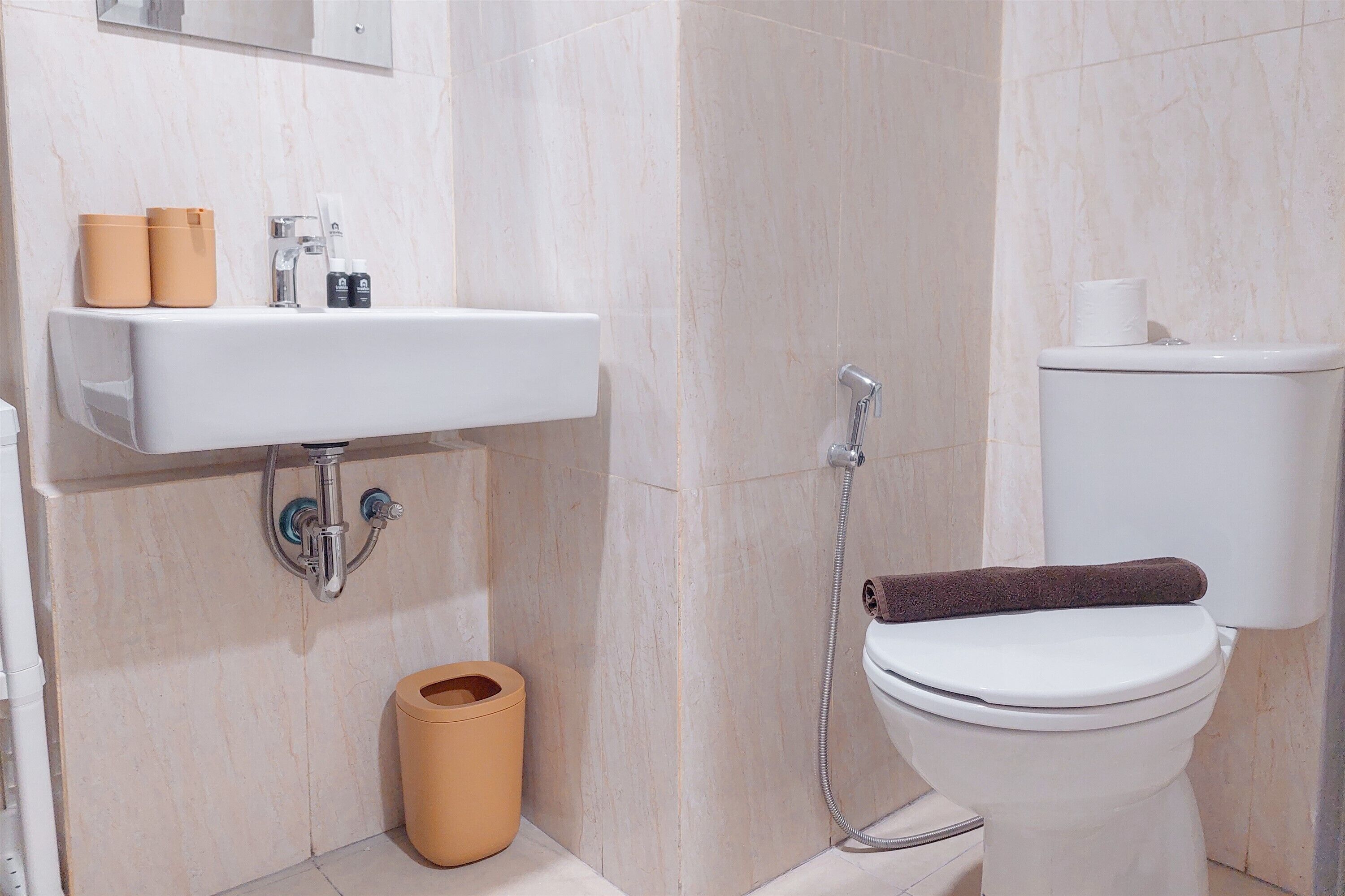 Kylpyhuoneessa on valkoinen pesuallas, wc-istuin ja suihku. Pesualtaalla on hygieniatuotteita ja wc-istuimen päällä pyyhe.