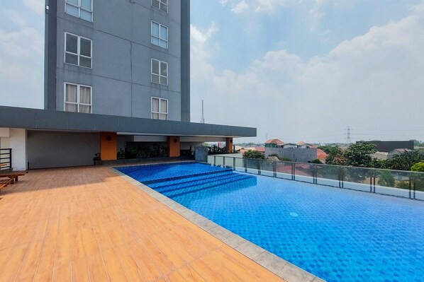 A rooftop pool with a wooden deck and a modern building in the background.