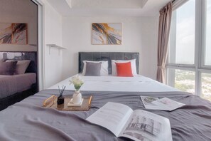 A hotel room with a bed, a reading area with a book and a magazine, a vase with flowers, and a window with a view. - Good Studio And Comfortable 1Br At Tamansari Bintaro Mansion Apartment (South Tangerang)