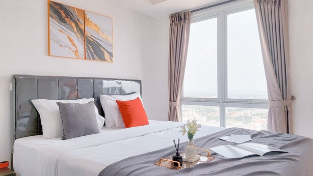A neatly made bed with a tray of items, a window with curtains, and a city view. - Good Studio And Comfortable 1Br At Tamansari Bintaro Mansion Apartment (South Tangerang)