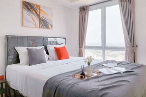 A neatly made bed with a tray of items, a window with curtains, and a city view. - Good Studio And Comfortable 1Br At Tamansari Bintaro Mansion Apartment (South Tangerang)