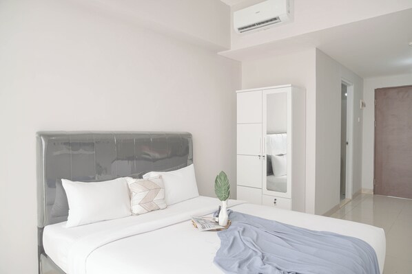 A modern bedroom with a large bed, white bedding, a grey headboard, a white wardrobe, and a potted plant. - Best Deal And Homey Studio Apartment Majestic Point Serpong (Gading Serpong)