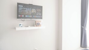 Ein Flachbildfernseher an der Wand montiert, darunter ein Regal mit einem Buch und einem kleinen dekorativen Gegenstand.