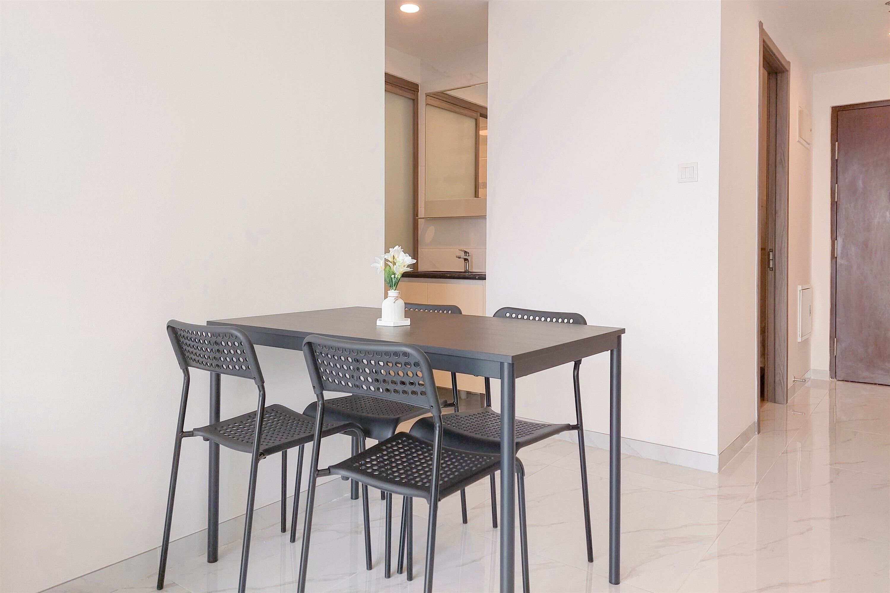 A dining area with a rectangular table and four chairs, a vase with flowers, and a kitchen visible in the background.