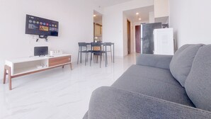 A modern living room with a grey sofa, a TV mounted on the wall, a dining area with a table and chairs, and a white cabinet. - Good Choice And Comfy 2Br Sky House Bsd Apartment (Pagedangan)