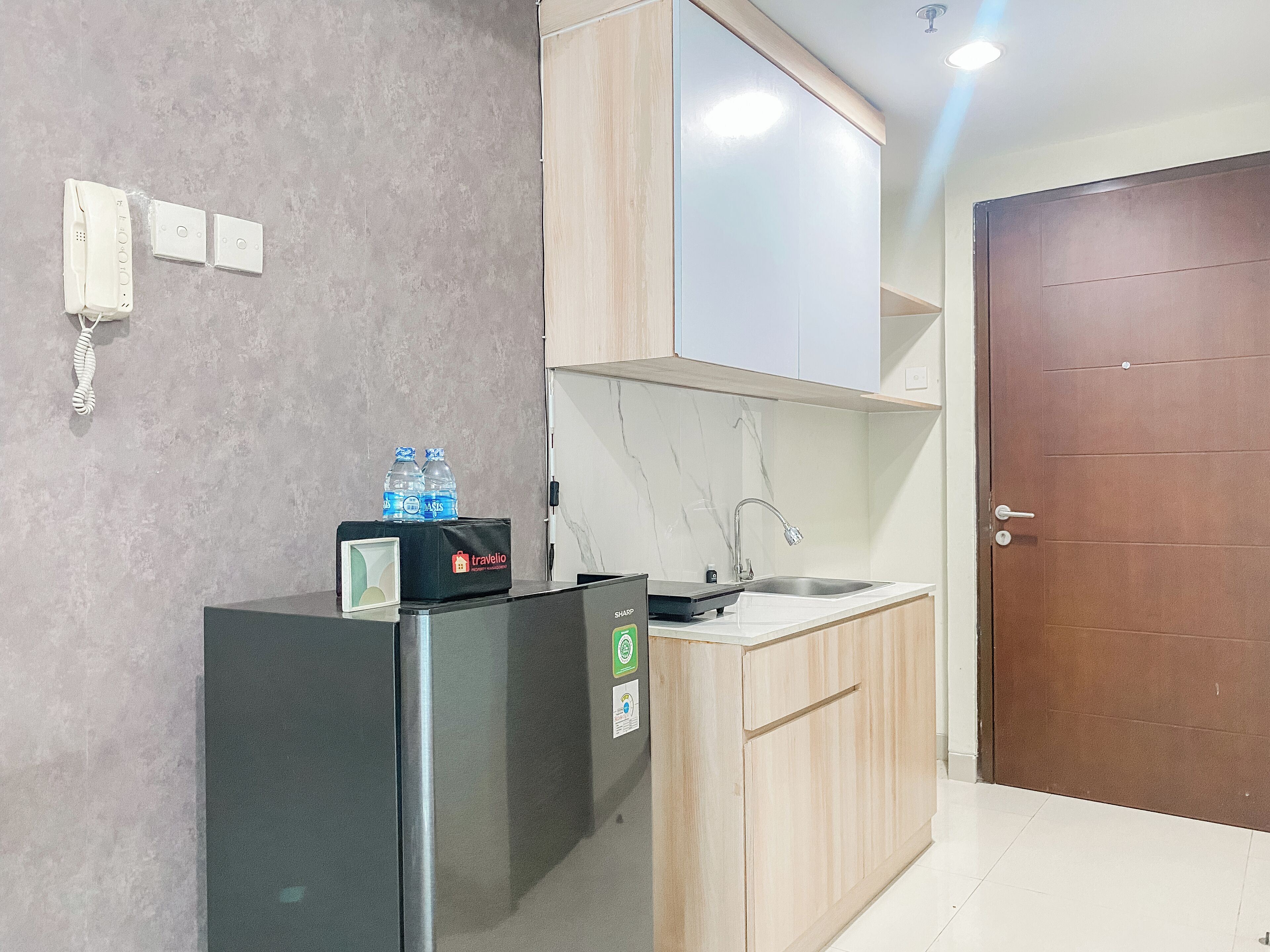 A compact kitchen with a refrigerator, a sink, and a wooden cabinet.
