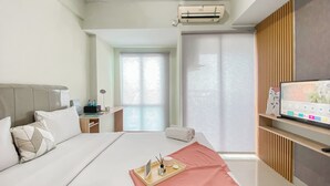 Una habitación de hotel moderna con una cama grande, un televisor sobre una estantería de madera, un escritorio con lámpara y una ventana con persianas.