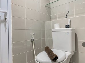 Clean and functional bathroom with a white toilet, glass shower enclosure, and large tile walls.