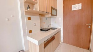 A small kitchen with wooden cabinets, a microwave, and a sink. There is a door with a sign on it.