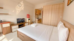 A modern hotel room with a large bed, wooden wardrobe, a small kitchenette, and a television on a wooden desk.