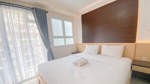 A neatly made bed with white linens and two pillows, a window with a view of buildings, and a wooden headboard. - Homey 1Br Apartment At Gateway Pasteur (Cimahi)