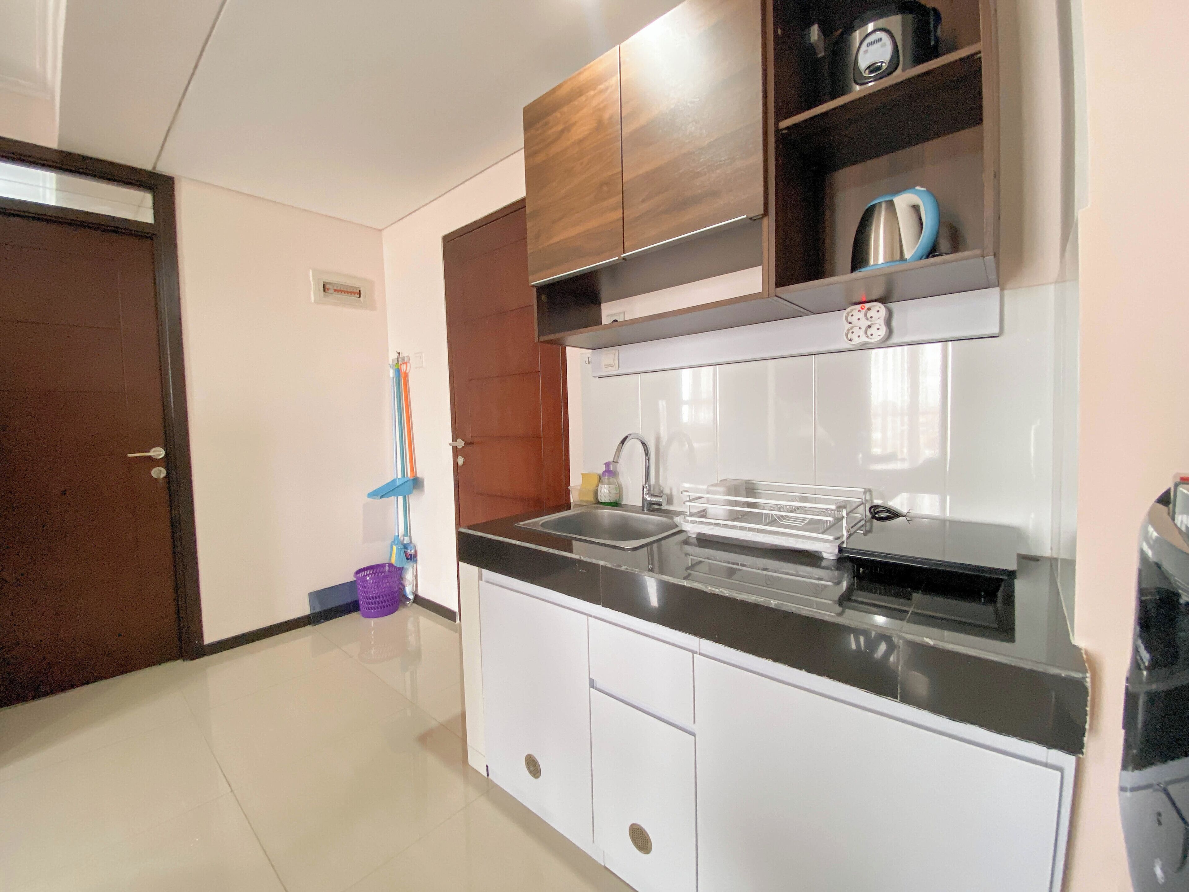 A modern kitchen with white cabinets, a black countertop, and a built-in oven. There is a sink and a kettle on the countertop.