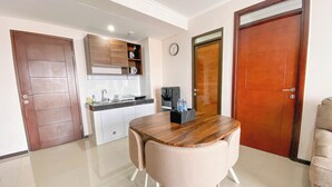Cozinha moderna com armários brancos, forno embutido e máquina de café. Há uma mesa de jantar com duas cadeiras no centro do cômodo.
