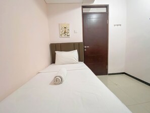A neatly made bed with a rolled towel, a brown door, and a small wall decoration. - Spacious And Minimalist 3Br At Gateway Pasteur Apartment (Cimahi)