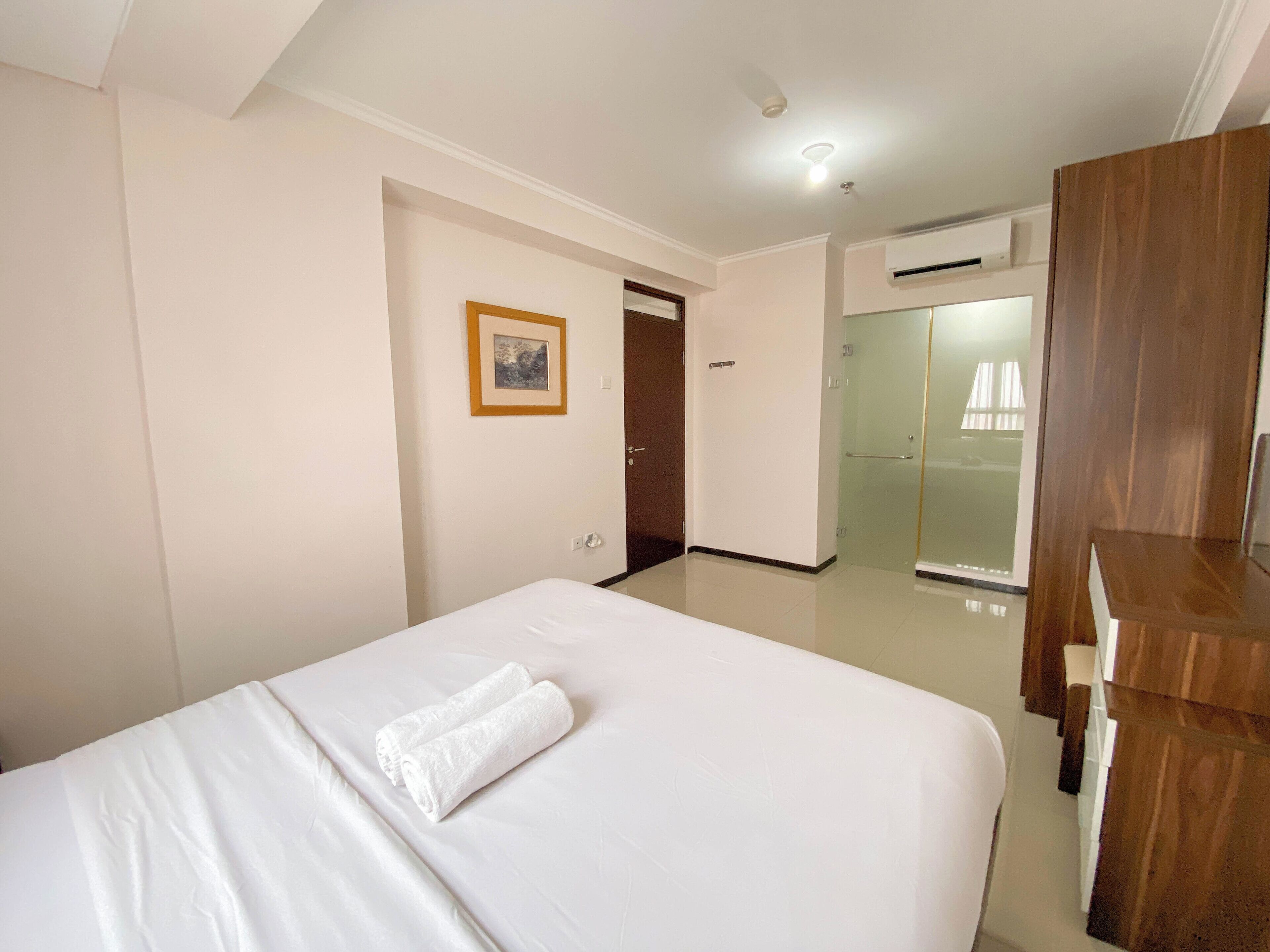 Une chambre d’hôtel avec un lit, une armoire en bois, une porte donnant sur une salle de bain et un tableau encadré au mur.