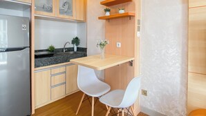 A compact kitchen with a refrigerator, cabinets, a sink, and a small table with two chairs. - Good Place And Spacious Studio Transpark Cibubur Apartment (Depok)